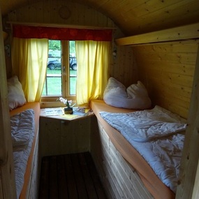 Gemütliches Holzhäuschen mit zwei Einzelbetten, gelben Vorhängen und Naturblick.