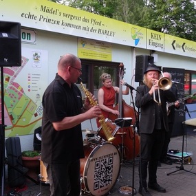 Eine Jazzband spielt live Musik mit Saxophon, Trompete und Kontrabass im Freien.