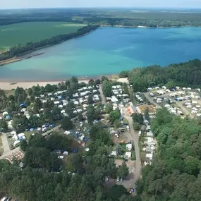 Luftaufnahme eines großen Campingplatzes am See mit Wohnmobilen, Bäumen und Sandstrand.