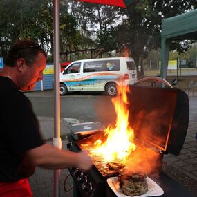Mann grillt Fleisch auf Gasgrill mit starker Flamme bei Grillfest im Freien.