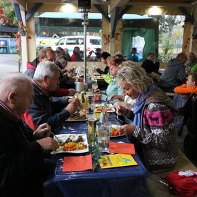 Gruppe älterer Menschen isst gemeinsam an langen Tischen bei einem geselligen Festessen.