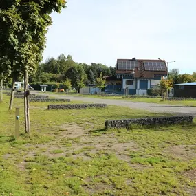 Stellplätze für Wohnmobile mit Bäumen und Haus mit Solaranlage auf grünem Campingplatz.