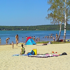 Familien genießen bei Sonnenschein einen Tag am Sandstrand an einem Badesee.